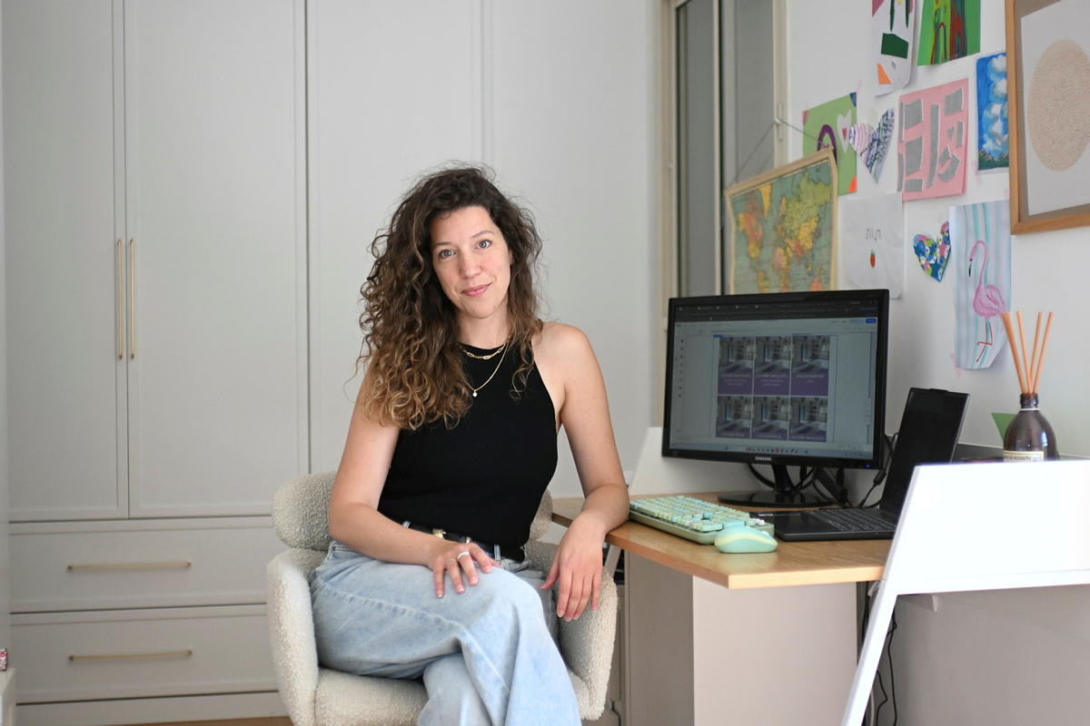 דנה וסרמן יושבת על כיסא לבן ליד שולחן עבודה עם מחשב ומחייכת